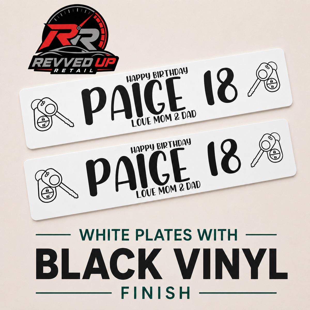 Two white personalized license plates with black text and icons, shown on a beige background with the Revved Up Retail logo and text reading 'White plates with black vinyl finish.'.