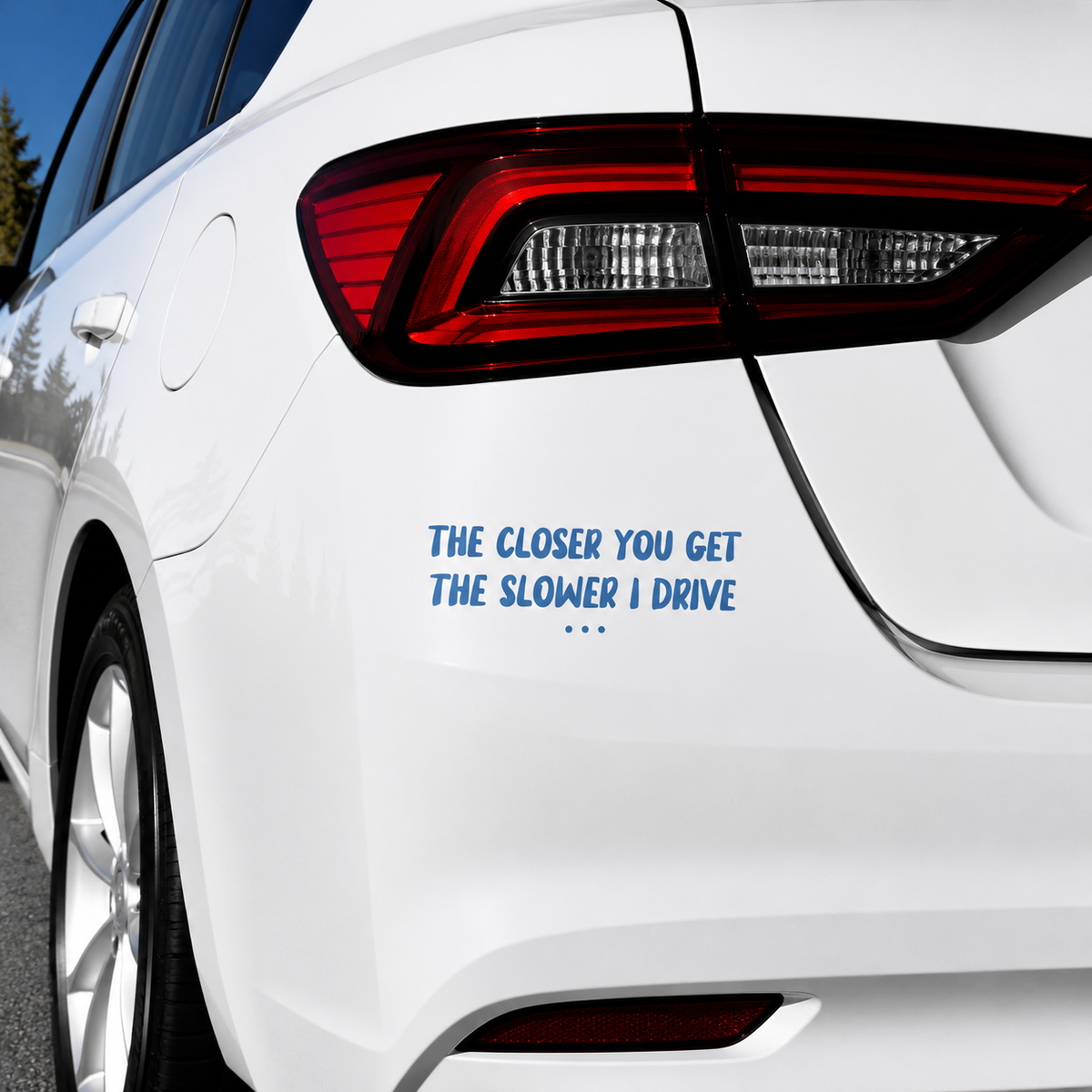 A blue vinyl car decal with the text 'THE CLOSER YOU GET THE SLOWER I DRIVE' applied to the rear left side of a white sedan.