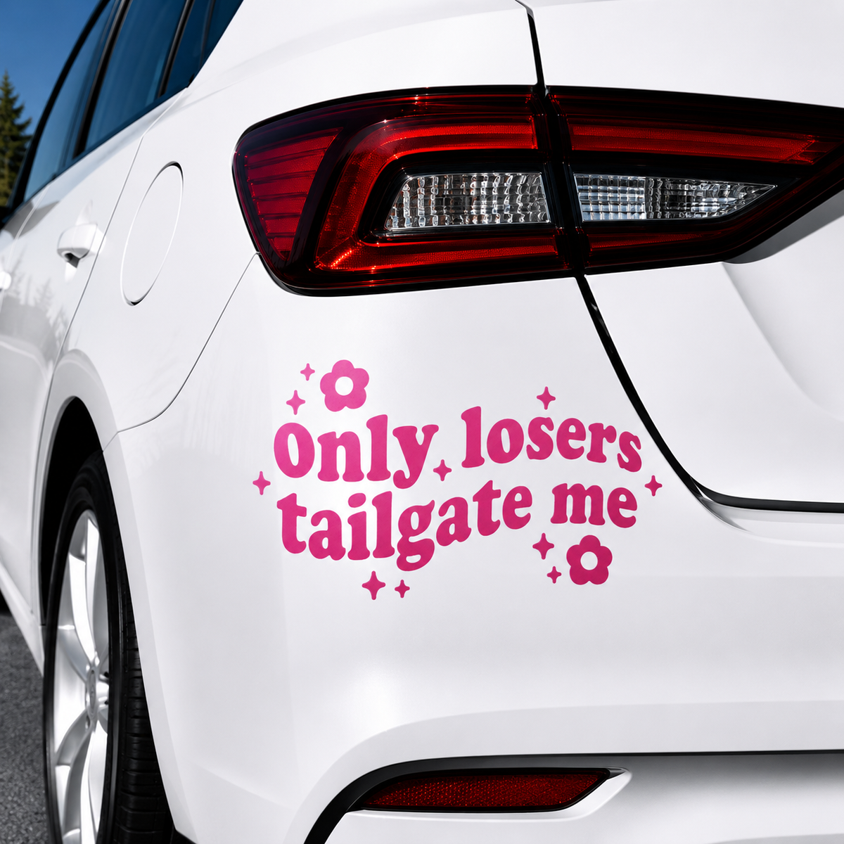 A pink vinyl car decal with the text 'Only losers tailgate me' and small flower and star accents, shown applied to the rear quarter panel of a white car.