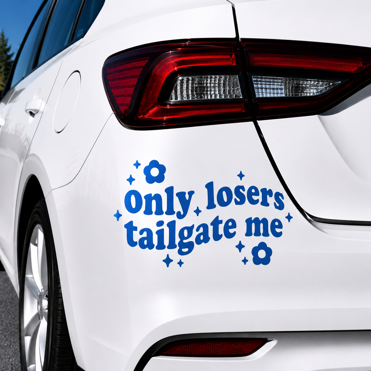 A blue vinyl car decal with the text 'Only losers tailgate me' surrounded by small blue flowers and star shapes, shown applied to the rear left side of a white car.