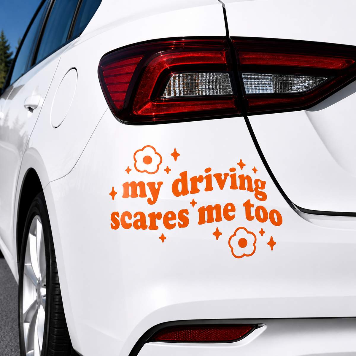 An orange vinyl car decal with the text 'my driving scares me too' and flower graphics, shown applied to the rear quarter panel of a white car.