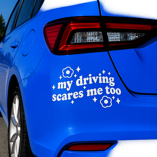 A white vinyl car decal with the text 'my driving scares me too' and small flower and star graphics, shown applied to the rear quarter panel of a bright blue car.