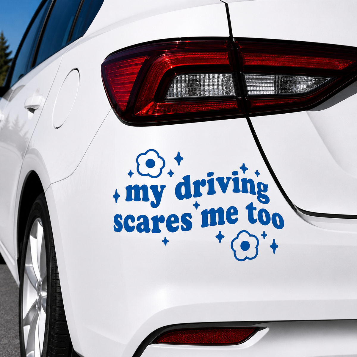 A blue vinyl car decal with the text 'my driving scares me too' and small flower and star graphics, shown applied to the rear quarter panel of a white car.