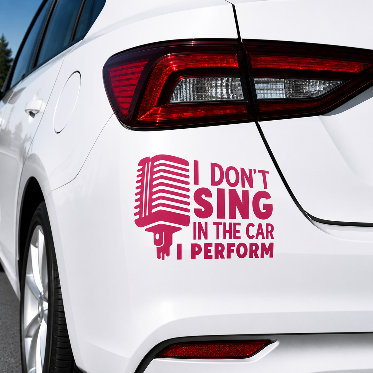 A pink vinyl decal applied to the rear quarter panel of a white car. The decal features a retro microphone graphic next to the text 'I DON'T SING IN THE CAR I PERFORM'.