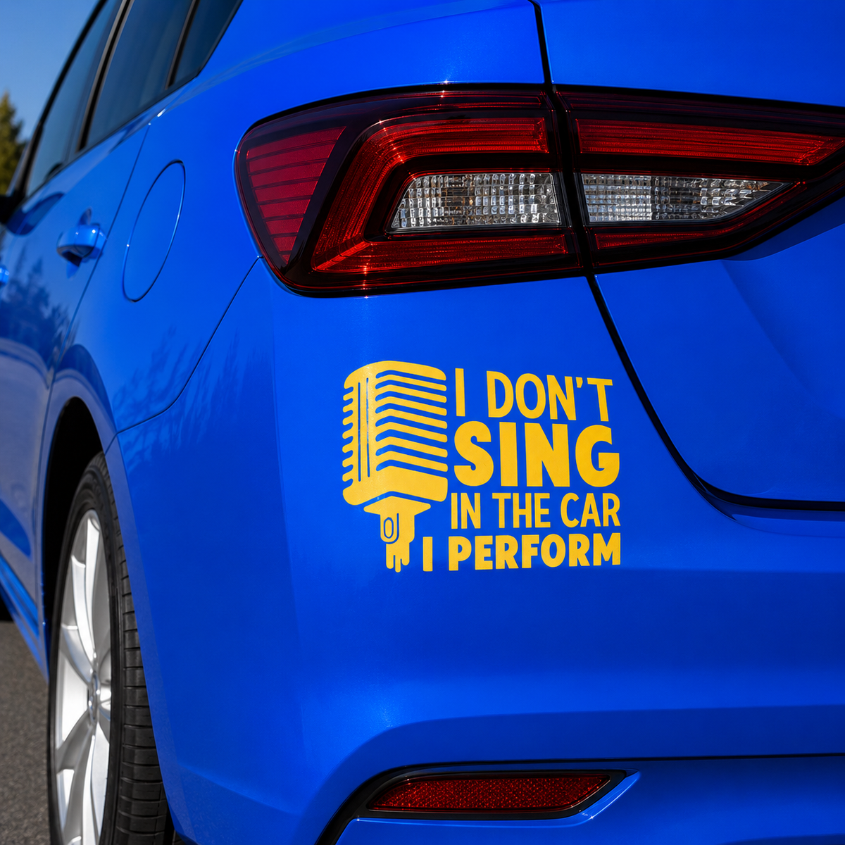 A yellow vinyl decal on the rear quarter panel of a blue car. The decal features a retro microphone graphic and the text 'I DON'T SING IN THE CAR I PERFORM'.