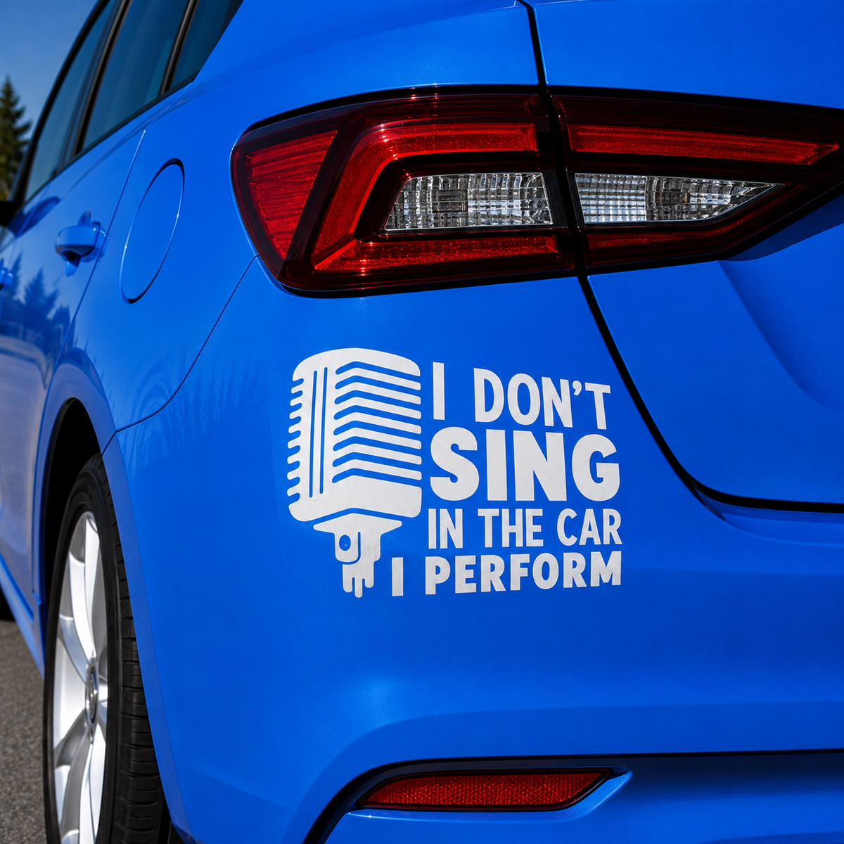 A white vinyl decal applied to the rear quarter panel of a bright blue car. The decal features a stylized microphone icon next to the text 'I DON'T SING IN THE CAR I PERFORM'.