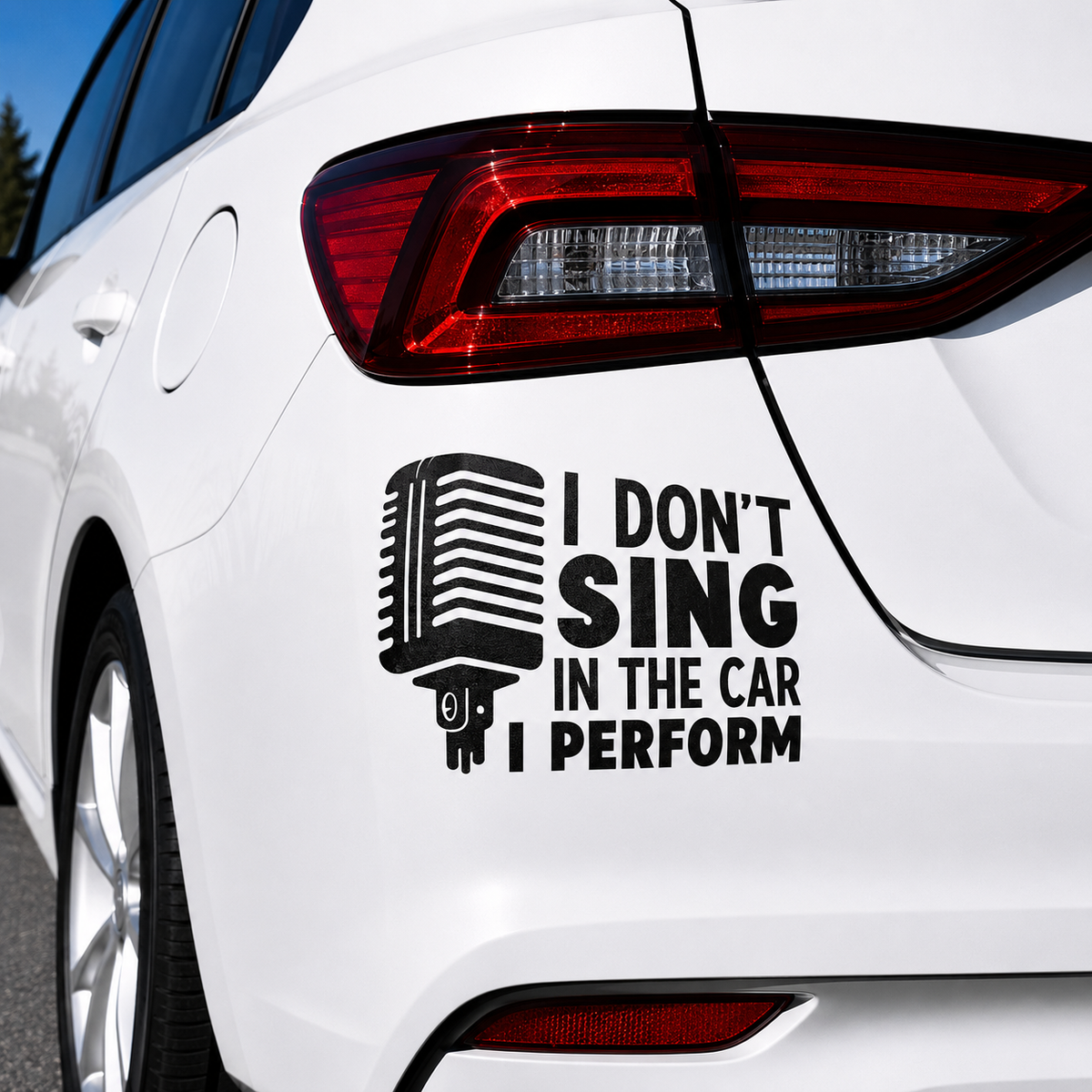 A black vinyl car decal applied to the rear quarter panel of a white car. The decal features a retro microphone graphic next to the text 'I DON'T SING IN THE CAR I PERFORM'.