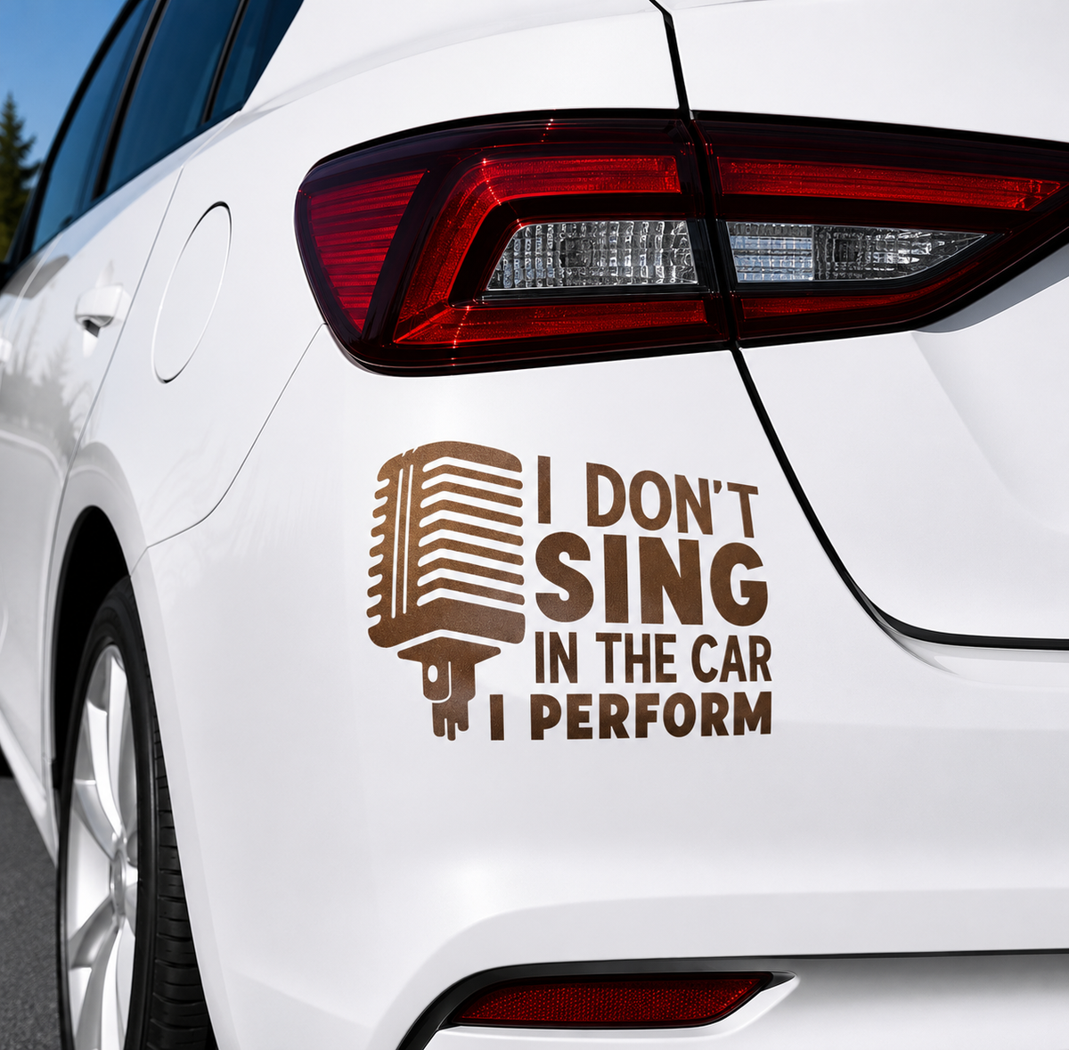 A brown vinyl decal applied to the rear quarter panel of a white car. The decal features a retro microphone icon on the left and the humorous text 'I DON'T SING IN THE CAR I PERFORM' on the right.
