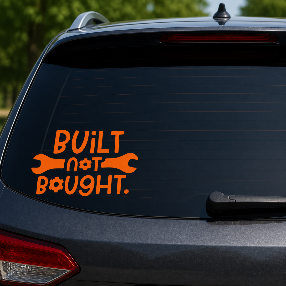 An orange vinyl decal on the rear window of a dark gray SUV. The decal features the text 'BUILT not BOUGHT.