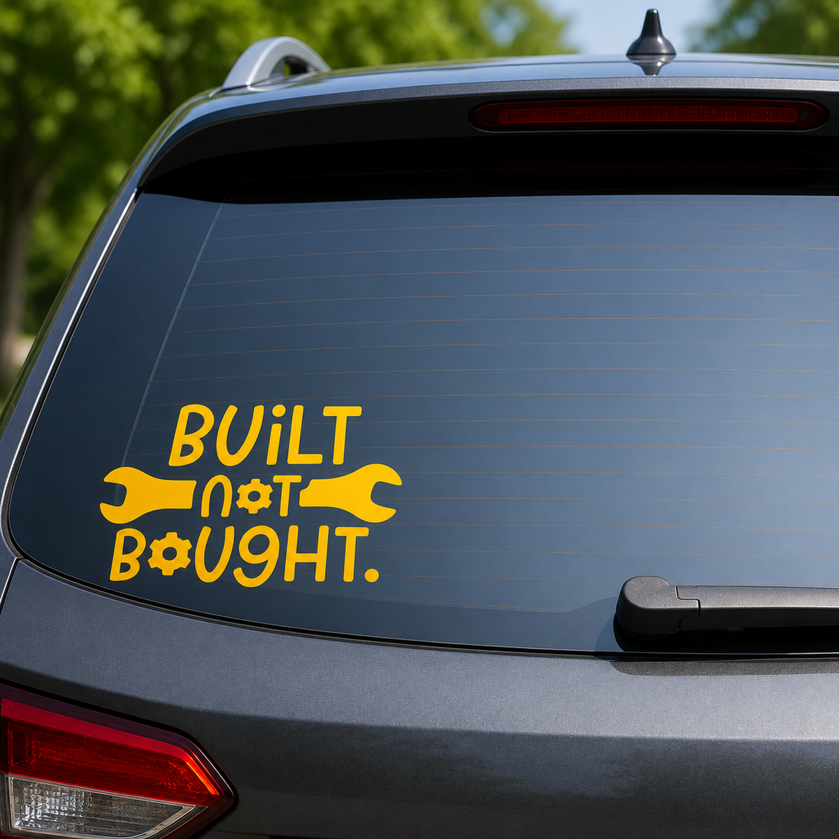 A yellow vinyl decal on the back window of a gray SUV, featuring the text 'BUILT NOT BOUGHT.' with wrench and gear icons.