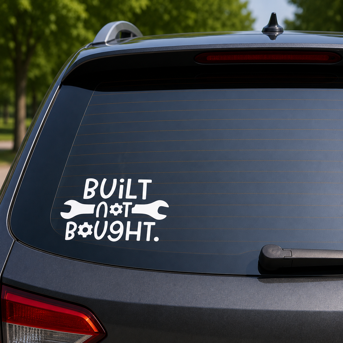 A white vinyl decal on the rear window of a dark gray SUV, featuring the text 'BUILT not BOUGHT.' with wrench and wrench-handles forming the letters.
