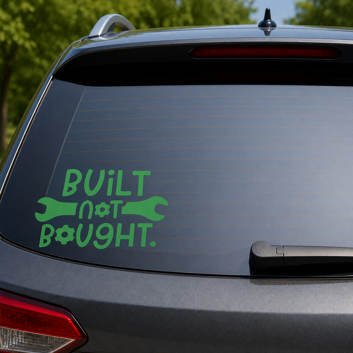 A green vinyl decal on the back window of a gray SUV, featuring the text 'BUILT not BOUGHT.' with wrench and gear icons.