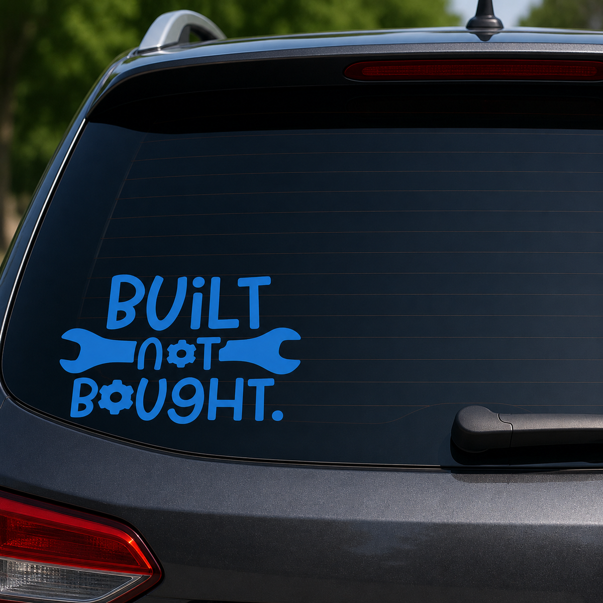 A blue vinyl decal on the rear window of a dark gray SUV, featuring the text 'BUILT not BOUGHT.' with wrench and gear icons, set against a blurred outdoor background.