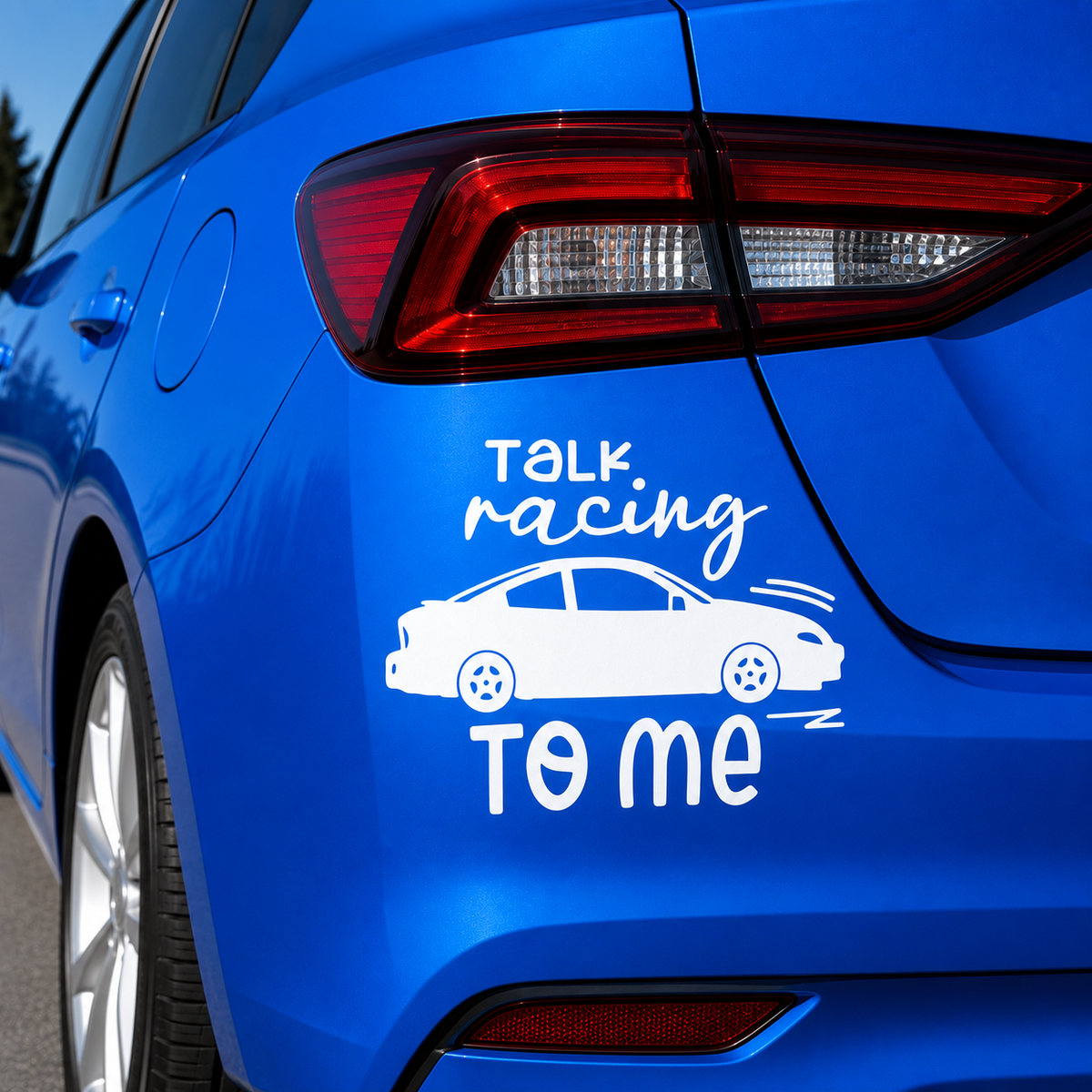 A white vinyl car decal with the text 'TALK racing TO ME' and a simple car silhouette, shown applied to the rear side panel of a bright blue car.