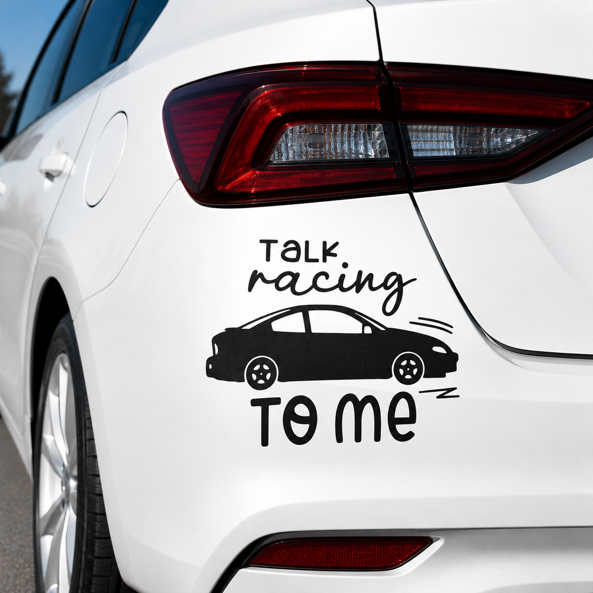 A black vinyl car decal applied to the rear quarter panel of a white sedan. The decal features the text 'TALK racing TO ME' in a stylized font, with a black silhouette of a sports sedan in the center.