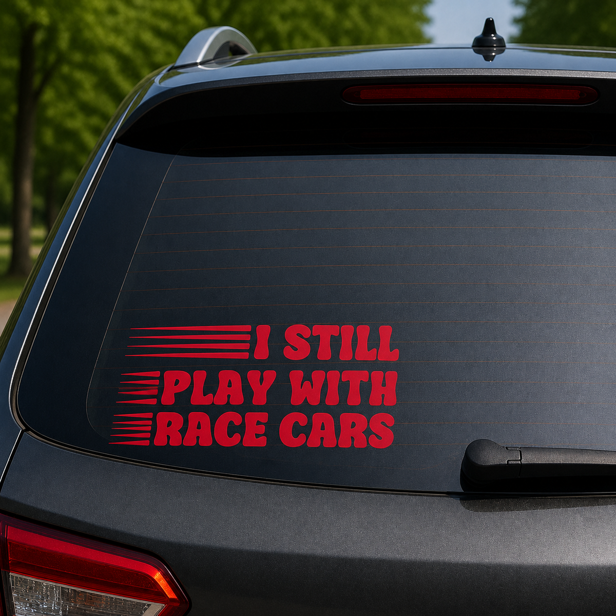A red vinyl decal on the rear window of a dark gray SUV, featuring the text 'I STILL PLAY WITH RACE CARS' with stylized racing stripes.