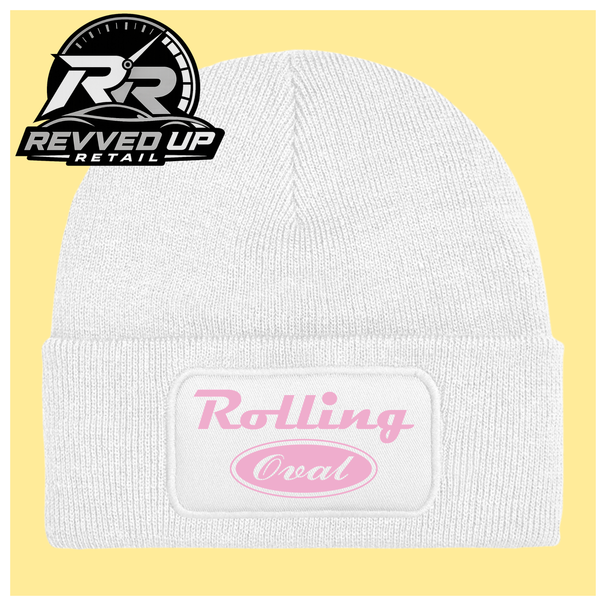 A white ribbed knit beanie with a folded cuff featuring a white patch that reads 'Rolling Oval' in pink script and oval lettering. The beanie is centered on a pale yellow background, with a Revved Up Retail logo in the top-left corner.