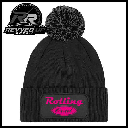 A black ribbed knit pom-pom beanie with a folded cuff featuring an oval black patch with hot pink text reading 'Rolling Oval'. A Revved Up Retail logo is visible in the top-left corner.