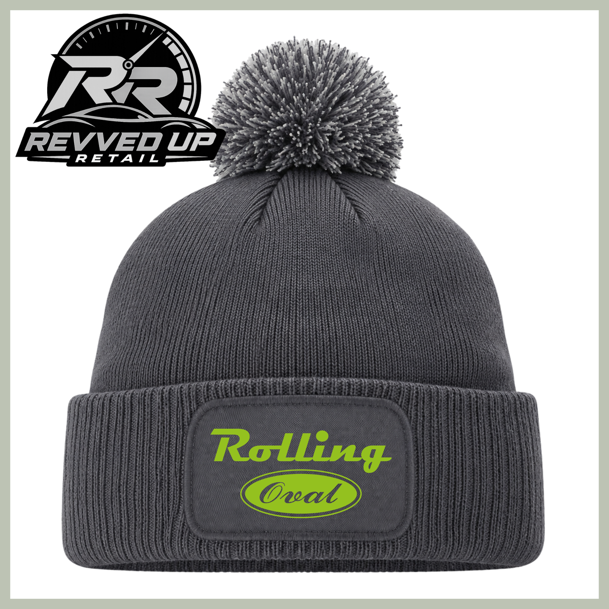 A dark gray ribbed knit beanie with a matching gray pom-pom and a folded cuff featuring a patch that reads 'Rolling Oval' in neon green. A Revved Up Retail logo is visible in the top-left corner.
