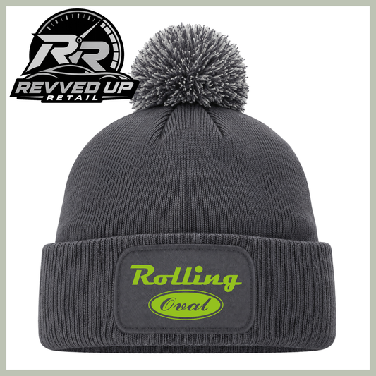 A dark gray ribbed knit beanie with a matching gray pom-pom and a folded cuff featuring a patch that reads 'Rolling Oval' in neon green. A Revved Up Retail logo is visible in the top-left corner.