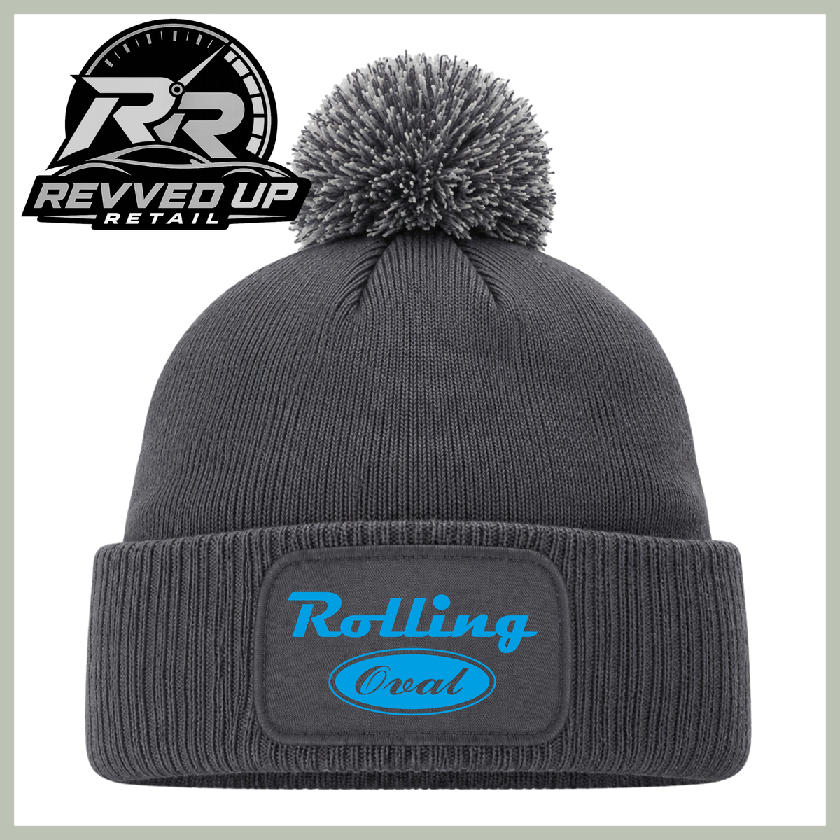 A dark gray ribbed knit beanie with a matching pom-pom and a cuffed brim featuring an oval patch with the words 'Rolling Oval' in blue. A Revved Up Retail logo is visible in the top-left corner.