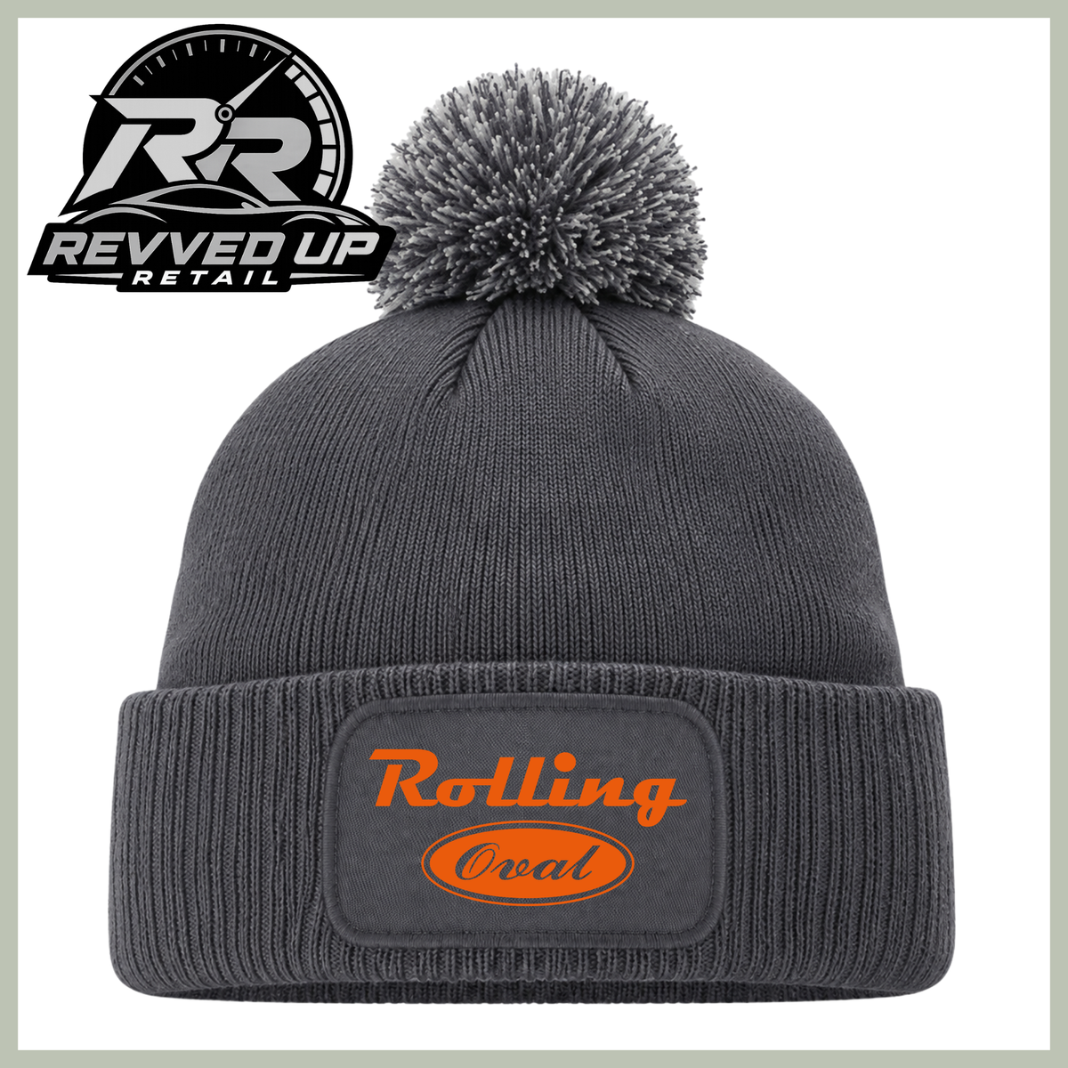 A dark gray ribbed knit beanie with a matching gray pom-pom on top and a folded cuff featuring a black patch with orange text that reads 'Rolling Oval.' A Revved Up Retail logo appears in the upper left corner.