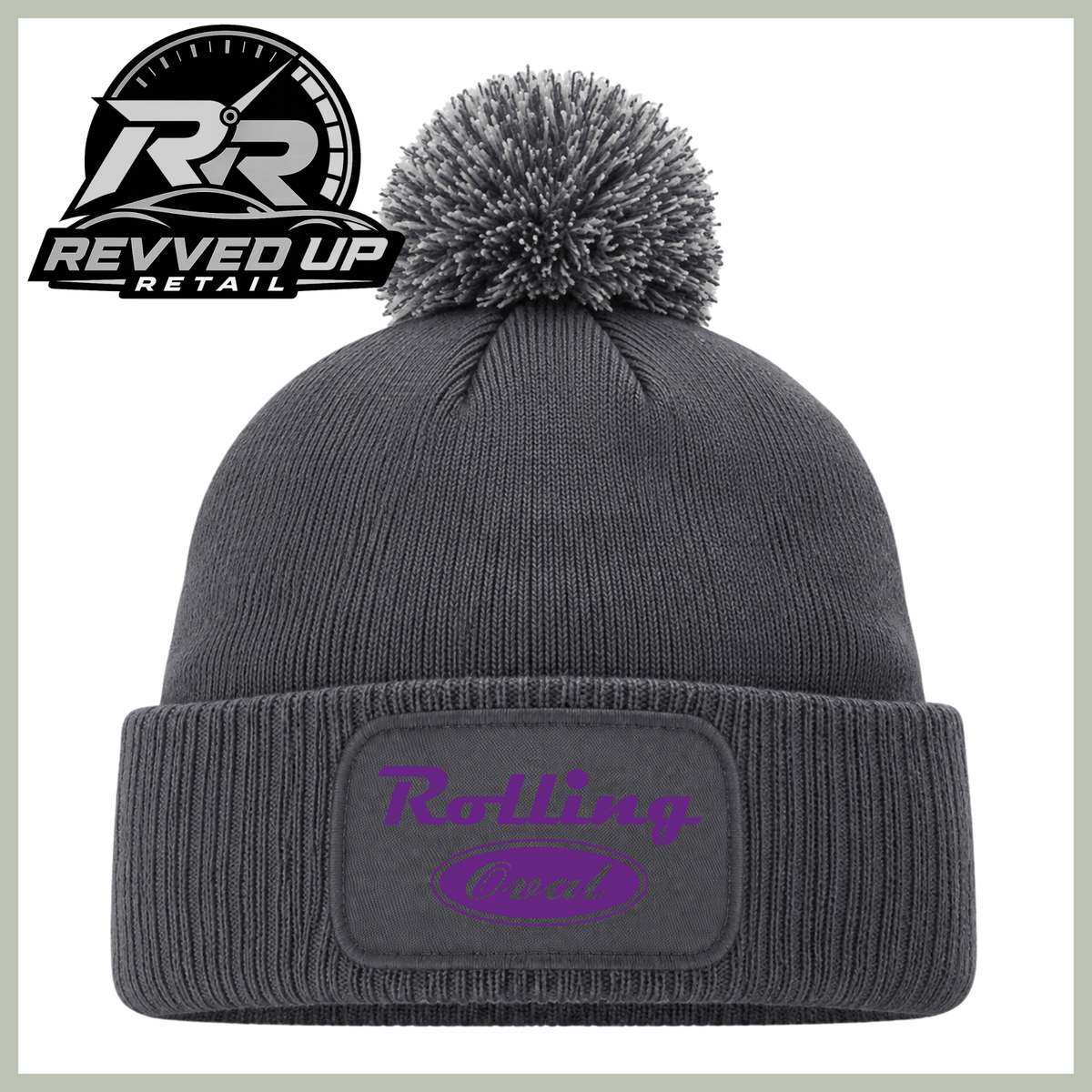 A dark gray ribbed knit pom-pom beanie with a cuffed brim, featuring a purple 'Rolling oval' logo patch on the front. The image includes a Revved Up Retail logo overlay in the top-left corner.
