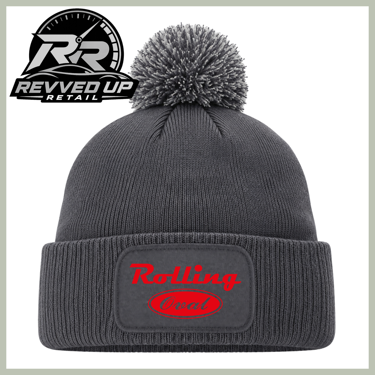 A dark gray ribbed knit pom-pom beanie with a cuffed brim, featuring a red 'Rolling oval' logo patch on the front. The image includes a Revved Up Retail logo overlay in the top-left corner.