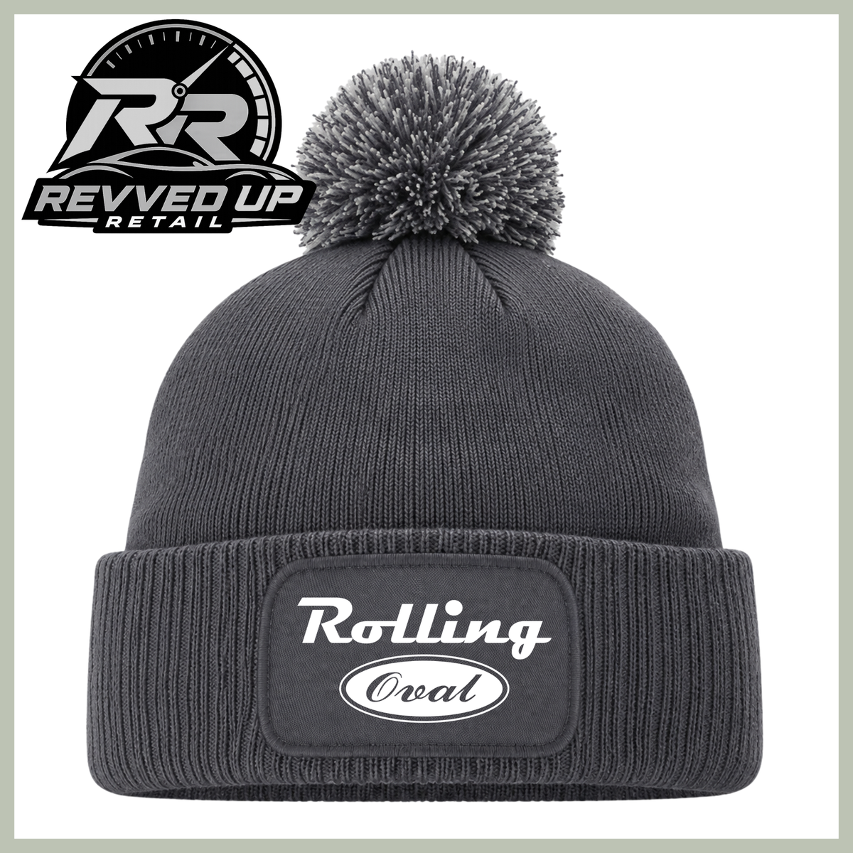 A dark gray ribbed knit pom-pom beanie with a cuffed brim, featuring a white 'Rolling oval' logo patch on the front. The image includes a Revved Up Retail logo overlay in the top-left corner.