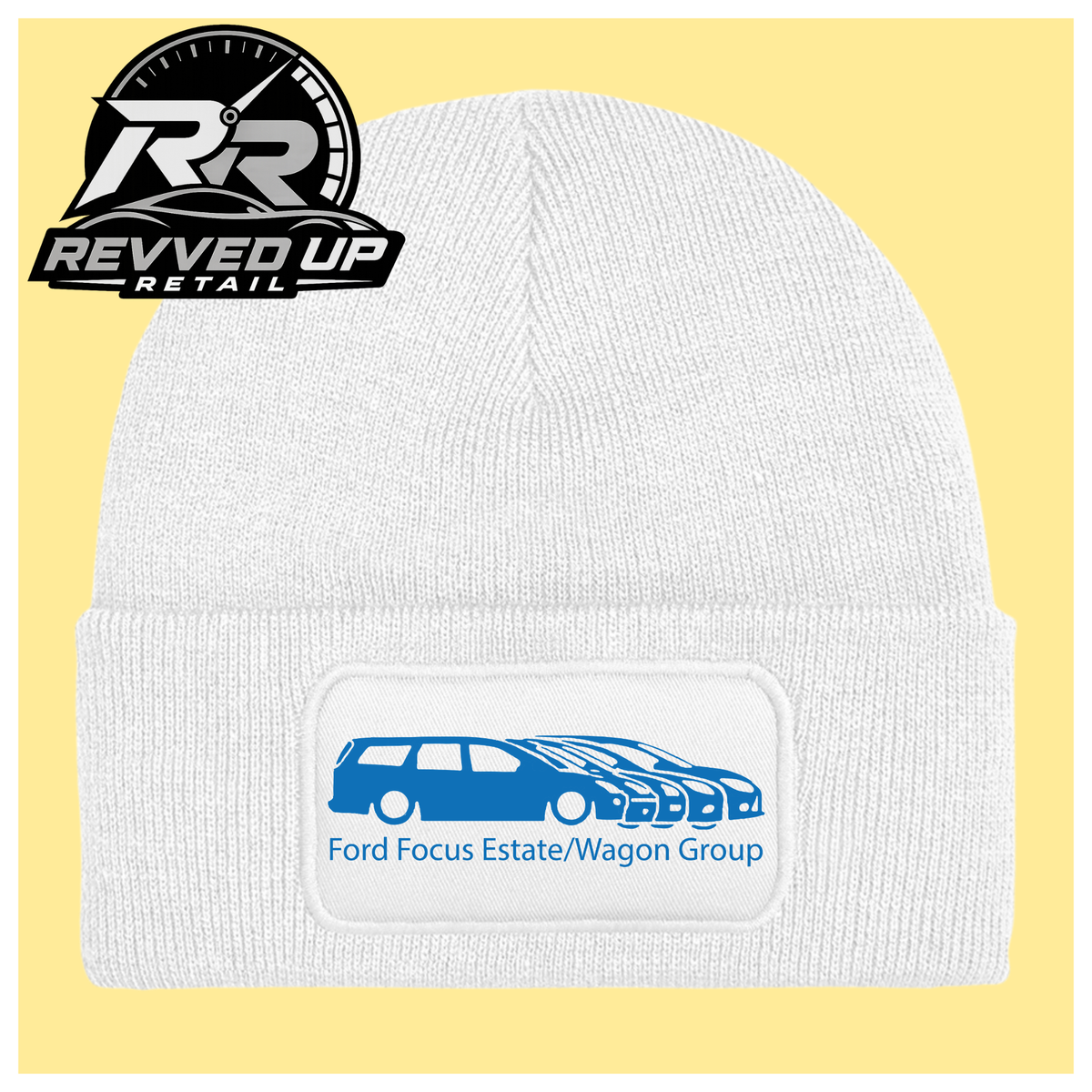 A white ribbed knit beanie with a folded cuff, featuring a black rectangular patch with a blue car graphic and the text 'Ford Focus Estate/Wagon Group.' A Revved Up Retail logo appears in the top-left corner.