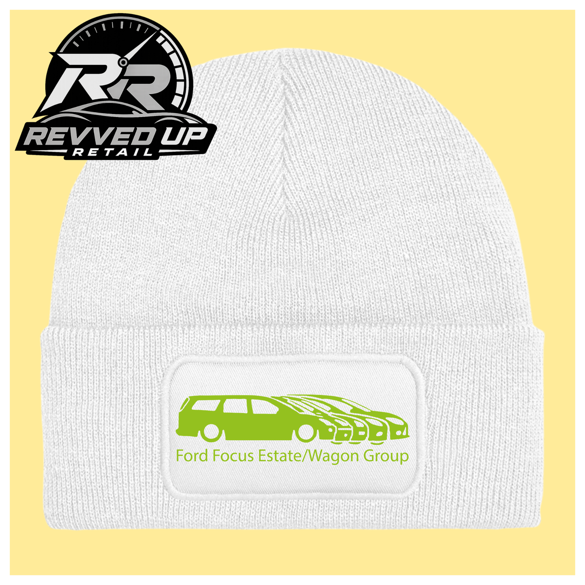 A white ribbed knit beanie with a folded cuff, featuring a black rectangular patch with a green car graphic and the text 'Ford Focus Estate/Wagon Group.' A Revved Up Retail logo appears in the top-left corner.
