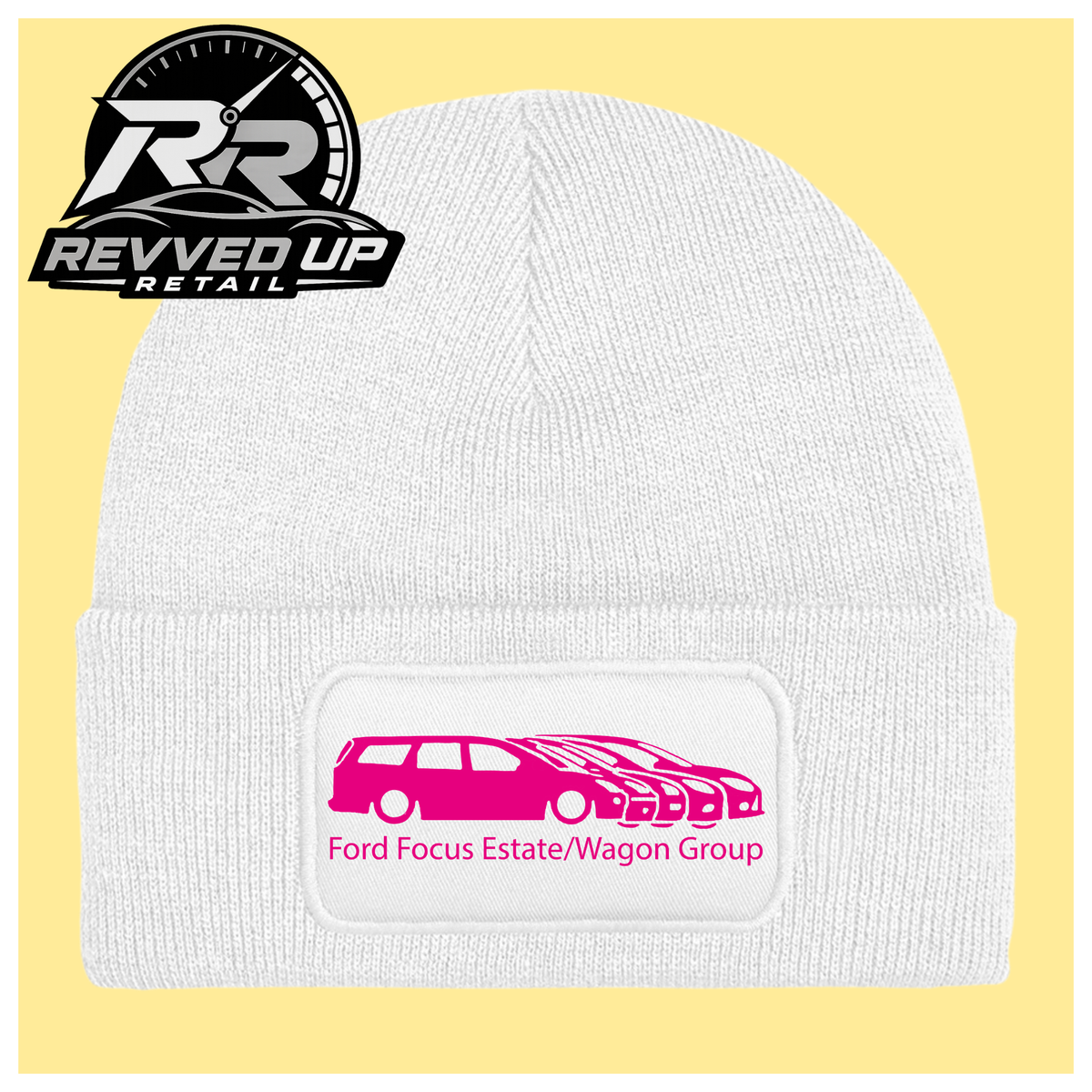 A white ribbed knit beanie with a folded cuff, featuring a black rectangular patch with a hot pink car graphic and the text 'Ford Focus Estate/Wagon Group.' A Revved Up Retail logo appears in the top-left corner.
