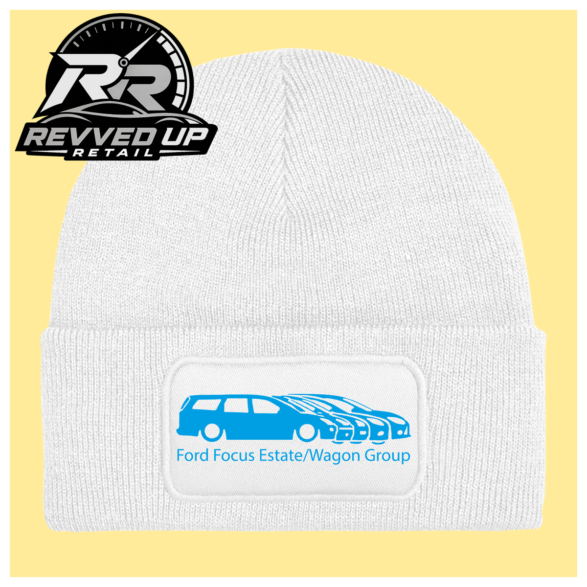 A white ribbed knit beanie with a folded cuff, featuring a black rectangular patch with a light blue car graphic and the text 'Ford Focus Estate/Wagon Group.' A Revved Up Retail logo appears in the top-left corner.