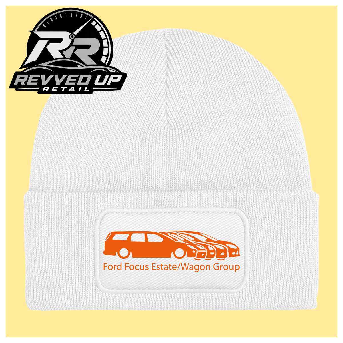 A white ribbed knit beanie with a folded cuff, featuring a black rectangular patch with a orange car graphic and the text 'Ford Focus Estate/Wagon Group.' A Revved Up Retail logo appears in the top-left corner.