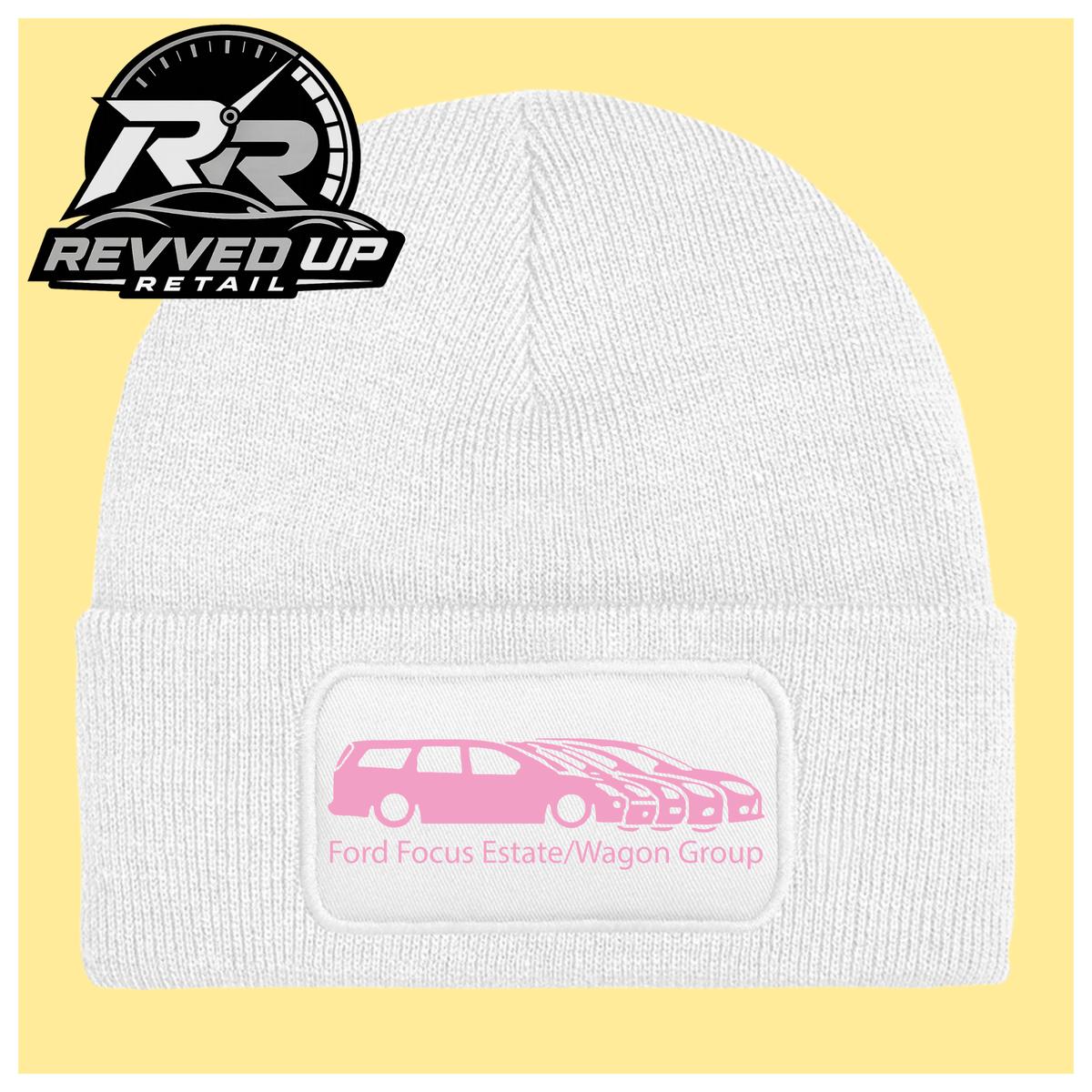 A white ribbed knit beanie with a folded cuff, featuring a black rectangular patch with a pale pink car graphic and the text 'Ford Focus Estate/Wagon Group.' A Revved Up Retail logo appears in the top-left corner.