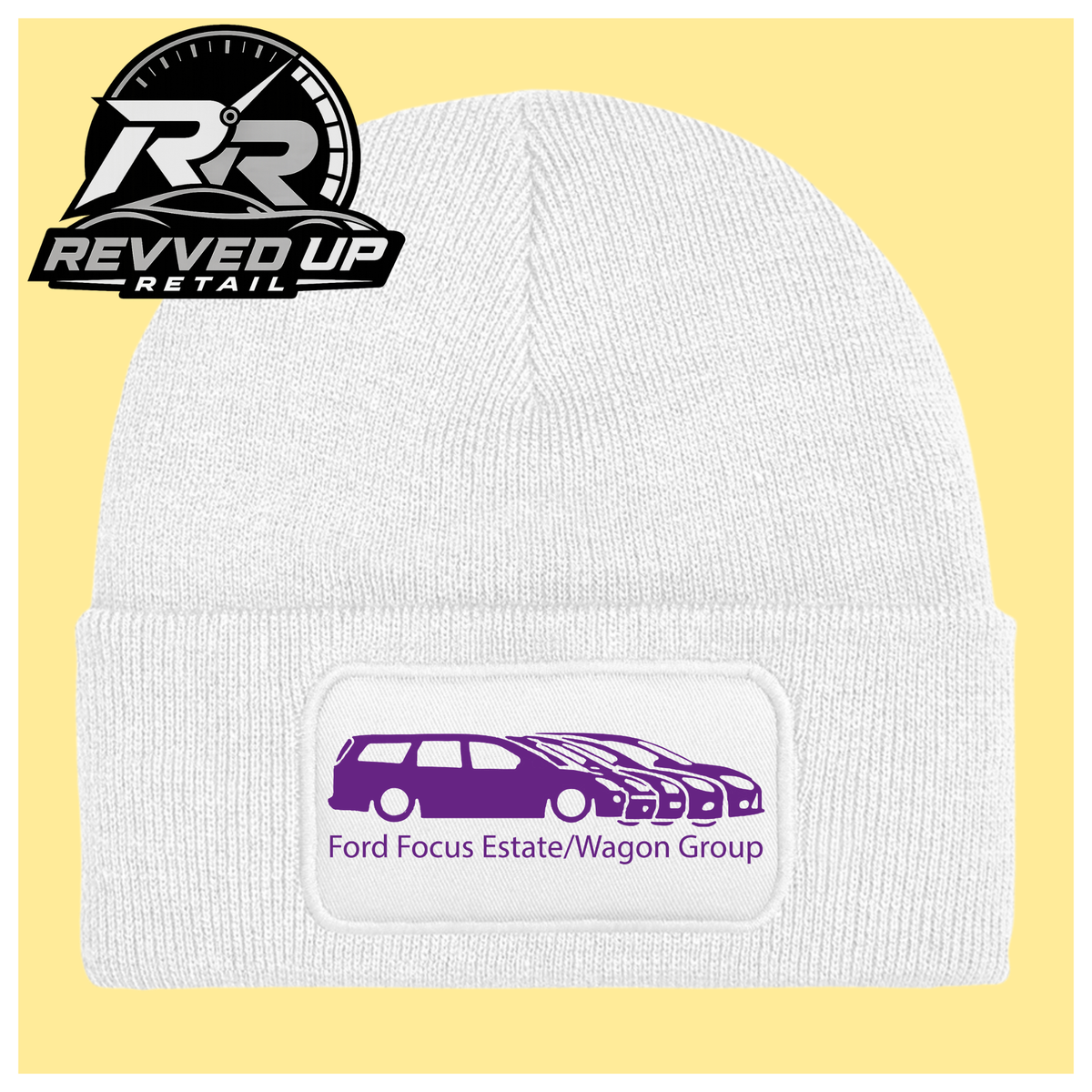 A white ribbed knit beanie with a folded cuff, featuring a black rectangular patch with a purple car graphic and the text 'Ford Focus Estate/Wagon Group.' A Revved Up Retail logo appears in the top-left corner.