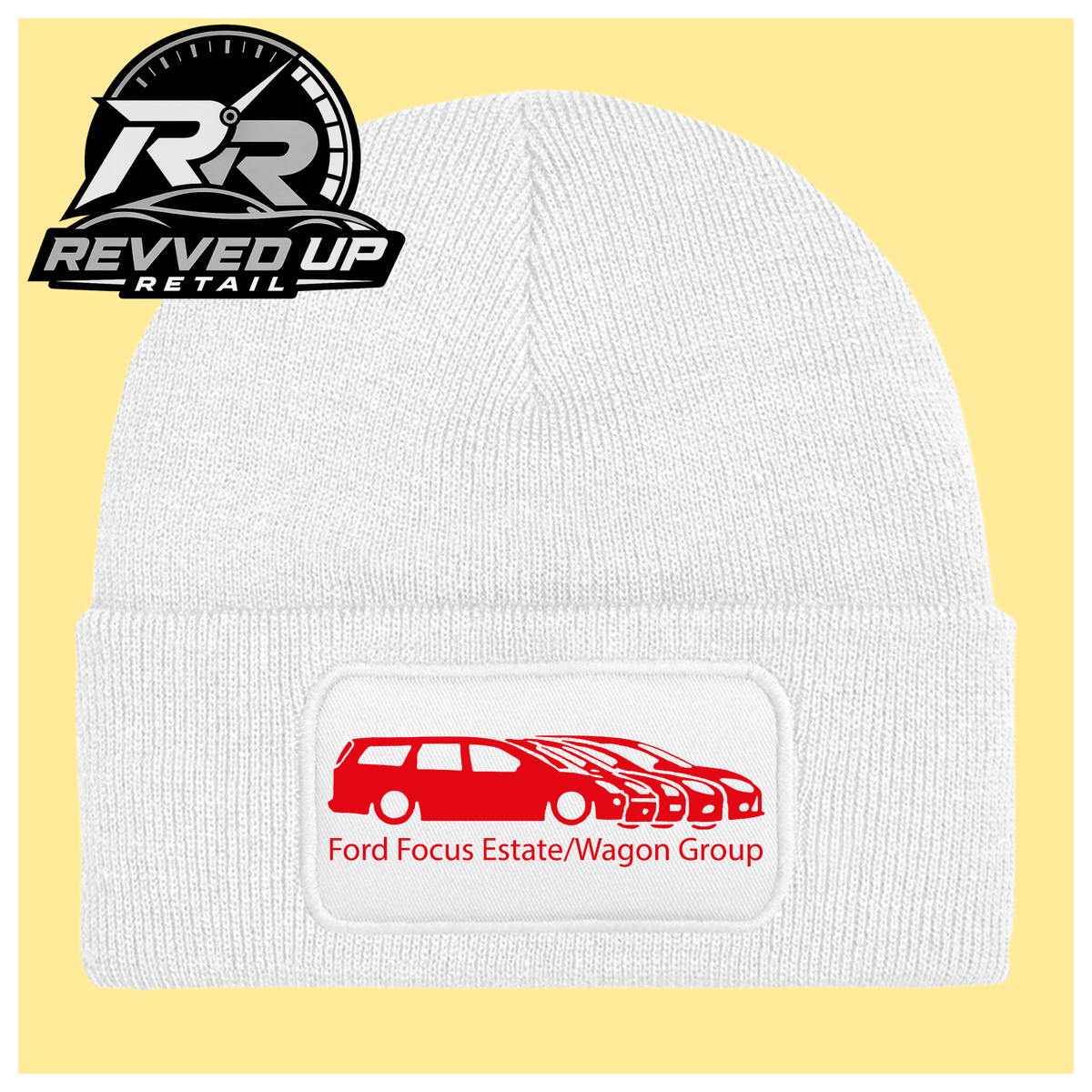 A white ribbed knit beanie with a folded cuff, featuring a black rectangular patch with a red car graphic and the text 'Ford Focus Estate/Wagon Group.' A Revved Up Retail logo appears in the top-left corner.