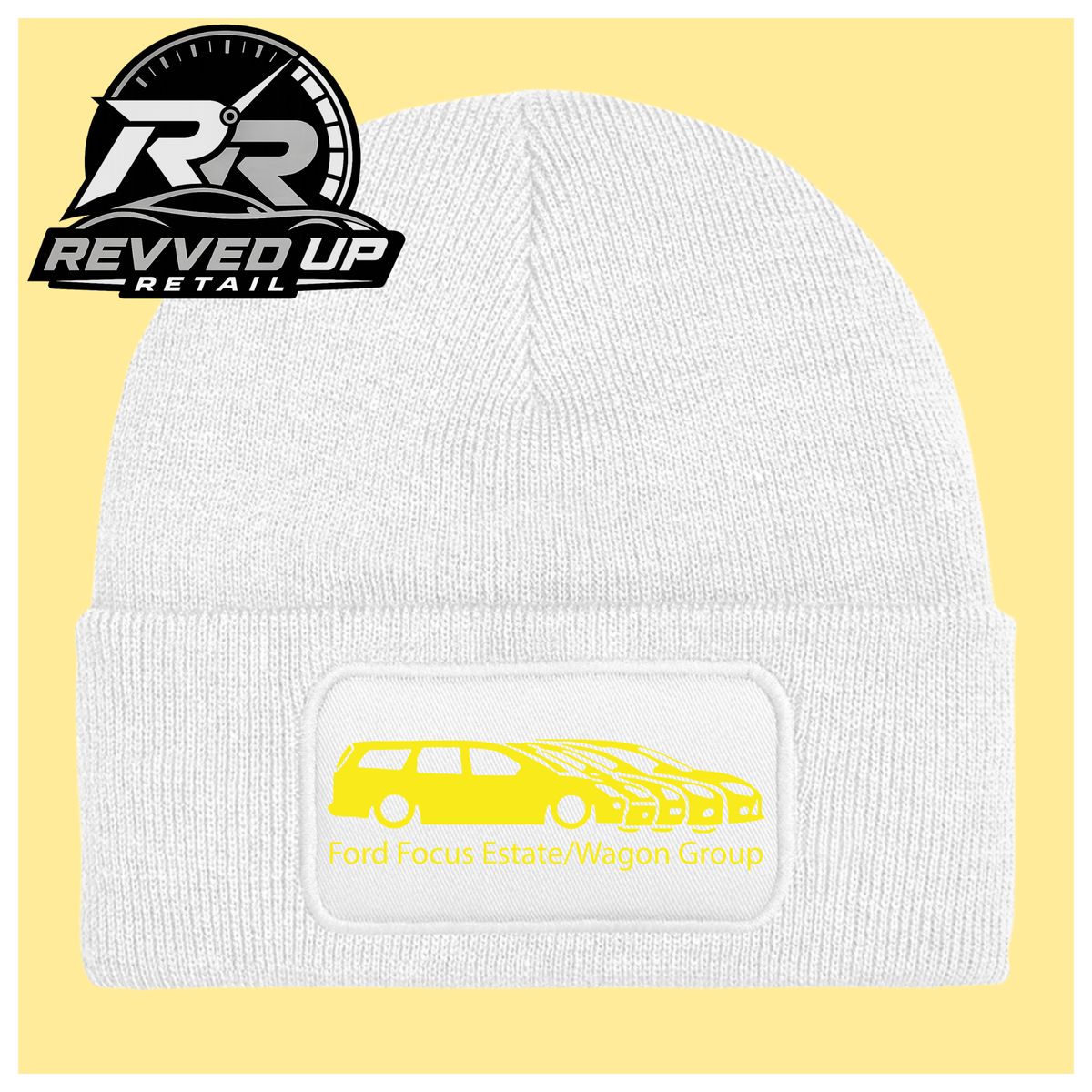 A white ribbed knit beanie with a folded cuff, featuring a black rectangular patch with a yellow car graphic and the text 'Ford Focus Estate/Wagon Group.' A Revved Up Retail logo appears in the top-left corner.