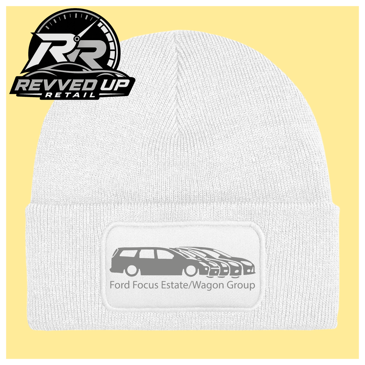 A white ribbed knit beanie with a folded cuff, featuring a black rectangular patch with a grey car graphic and the text 'Ford Focus Estate/Wagon Group.' A Revved Up Retail logo appears in the top-left corner.