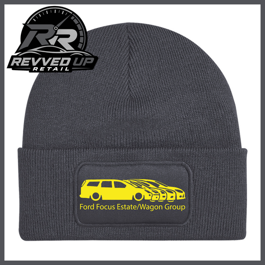 A grey ribbed knit beanie with a folded cuff, featuring a black rectangular patch with a yellow car graphic and the text 'Ford Focus Estate/Wagon Group.' A Revved Up Retail logo appears in the top-left corner.