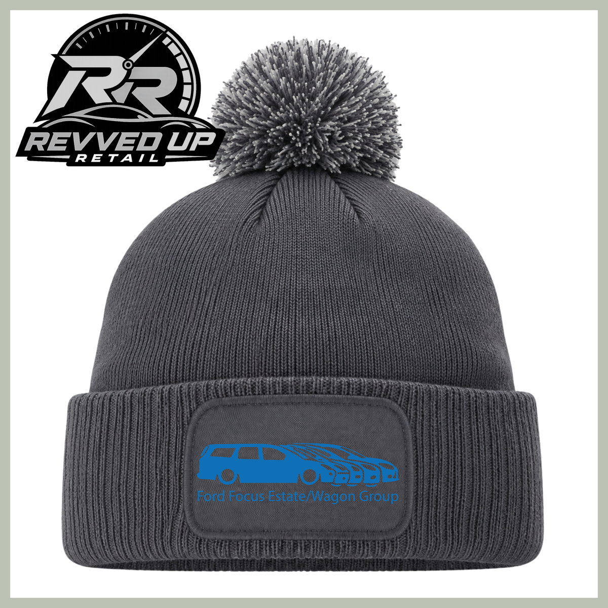 A dark gray ribbed knit beanie with a matching pom-pom and a folded cuff featuring a rectangular patch with a blue car graphic and the text 'Ford Focus Estate/Wagon Group.' A Revved Up Retail logo appears in the top-left corner.