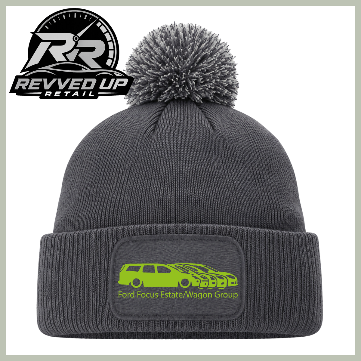 A dark gray ribbed knit beanie with a matching pom-pom and a folded cuff featuring a rectangular patch with a bright green car graphic and the text 'Ford Focus Estate/Wagon Group.' A Revved Up Retail logo appears in the top-left corner.