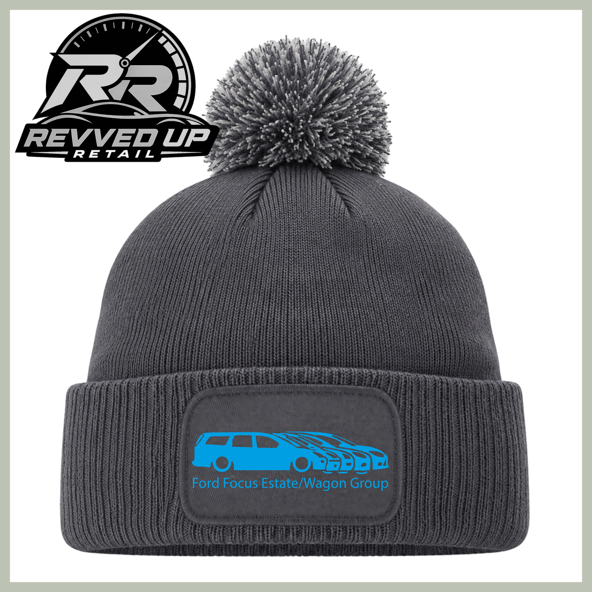 A dark gray knit pom-pom beanie with a folded cuff and a rectangular patch on the front featuring a blue car graphic and the text 'Ford Focus Estate/Wagon Group.' A Revved Up Retail logo appears in the top-left corner.