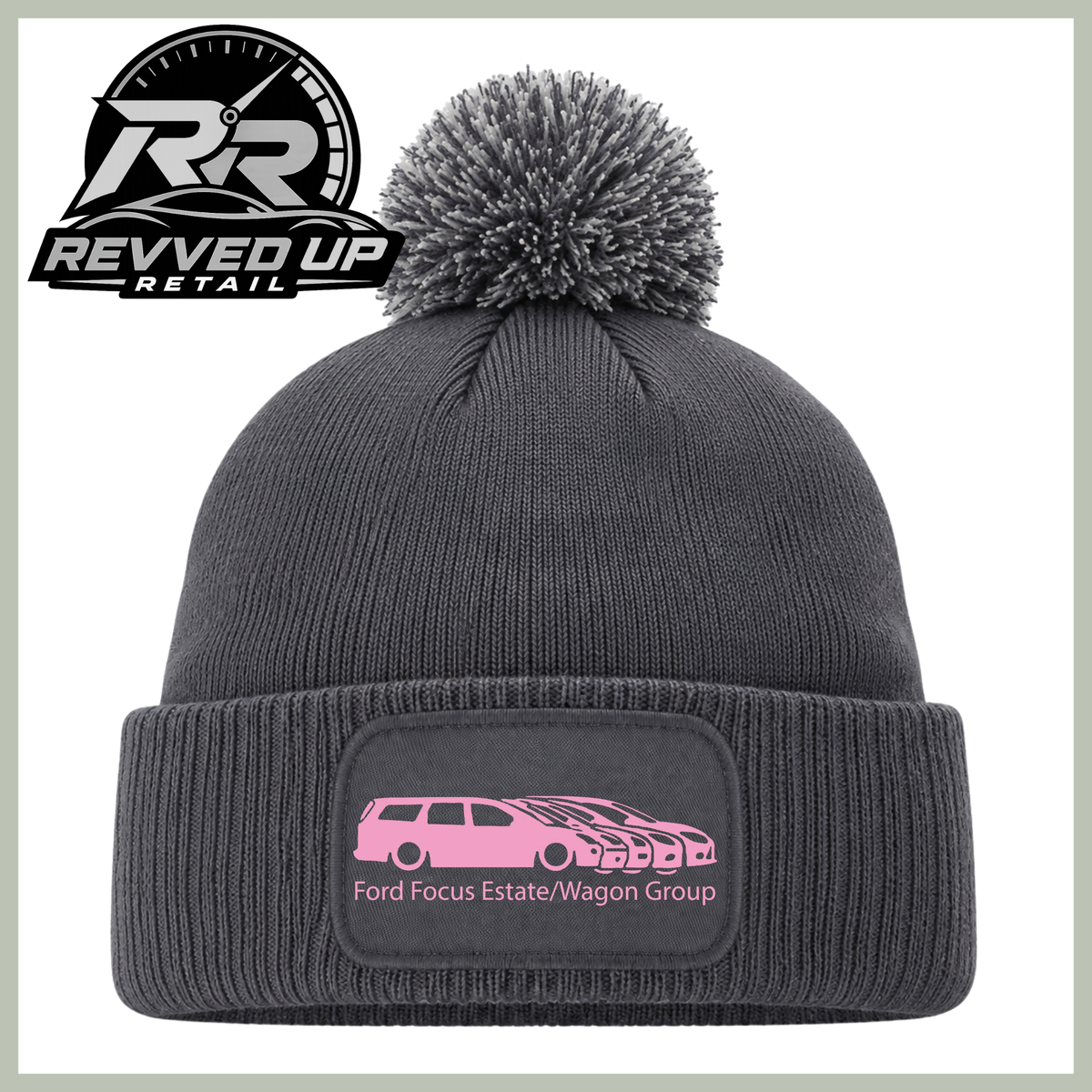 A dark gray ribbed knit beanie with a matching pom-pom on top and a folded cuff featuring a rectangular patch with a pink car graphic and the text 'Ford Focus Estate/Wagon Group.' A Revved Up Retail logo appears in the upper left corner.