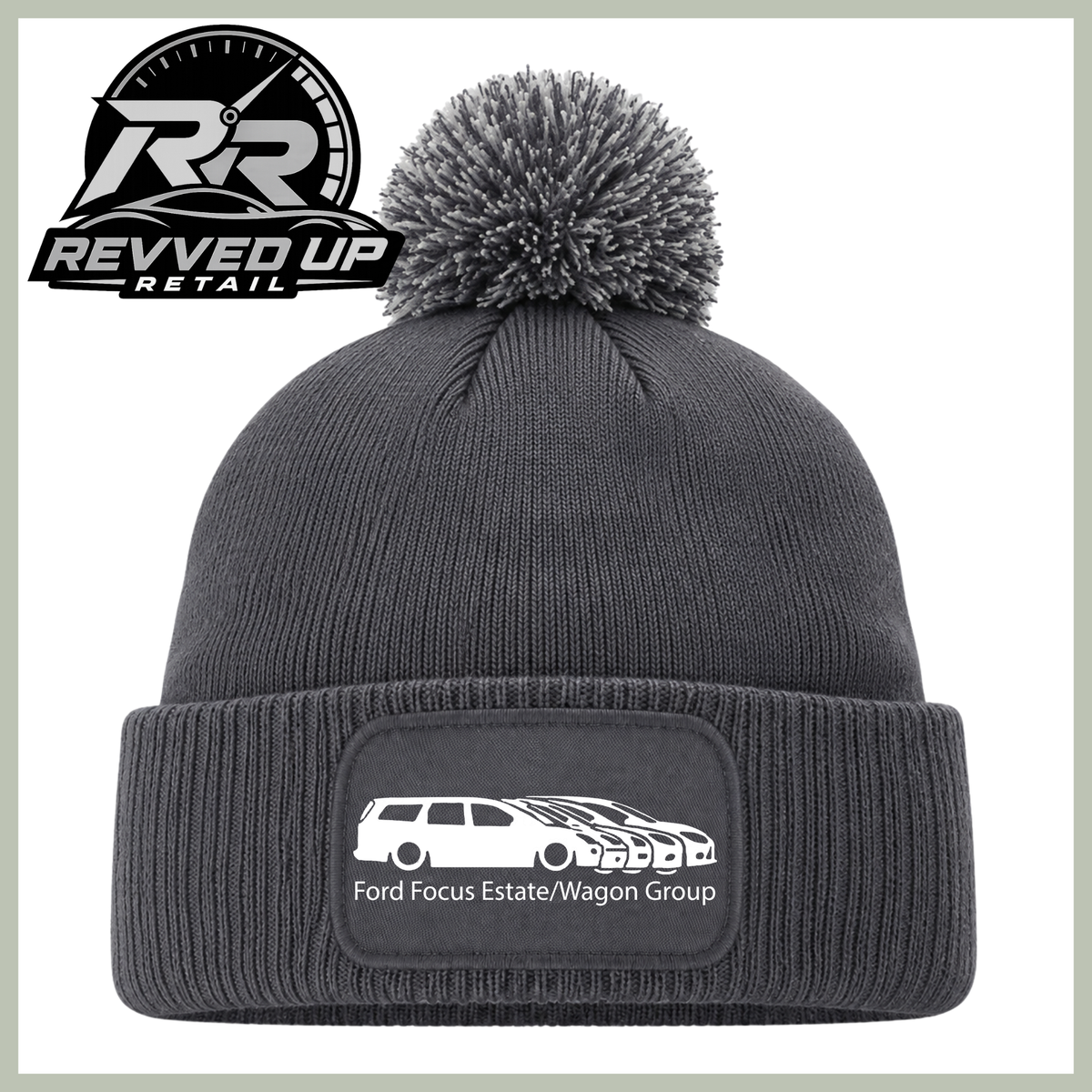 A dark gray ribbed knit beanie with a matching gray pom-pom on top and a folded cuff featuring a rectangular patch with a white car graphic and the text 'Ford Focus Estate/Wagon Group'. The Revved Up Retail logo is displayed in the upper left corner.