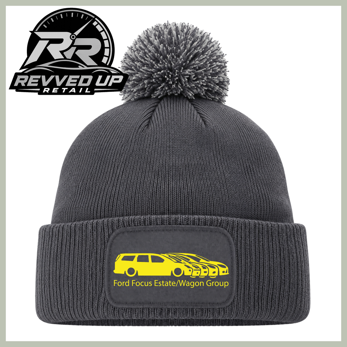A dark gray ribbed knit beanie with a matching gray pom-pom on top and a folded cuff featuring a rectangular patch with a yellow car graphic and the text 'Ford Focus Estate/Wagon Group'. The Revved Up Retail logo is displayed in the upper left corner.