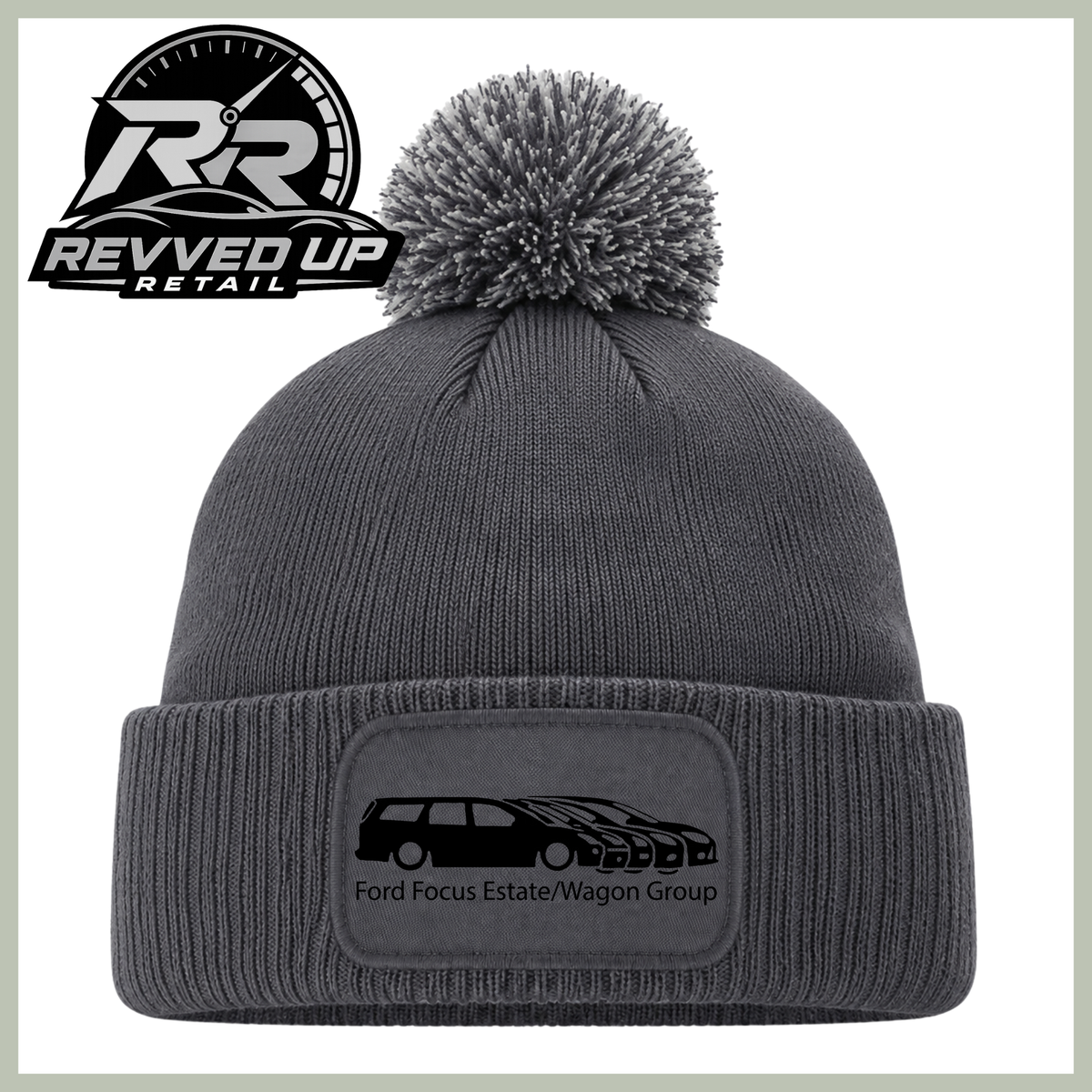 A dark gray ribbed knit beanie with a matching gray pom-pom on top and a folded cuff featuring a rectangular patch with a black car graphic and the text 'Ford Focus Estate/Wagon Group'. The Revved Up Retail logo is displayed in the upper left corner.