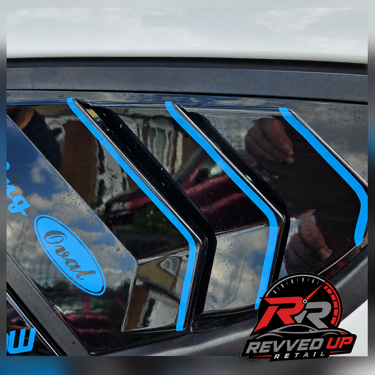 Blue oval window decals applied to the side window of a car, shown with reflections and a Revved Up Retail logo in the corner.