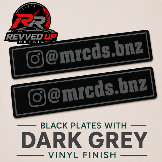 Two black rectangular vinyl decals with dark grey Instagram-style handles, shown on a light beige background with Revved Up Retail branding and text reading 'Black Plates with Dark Grey Vinyl Finish'.
