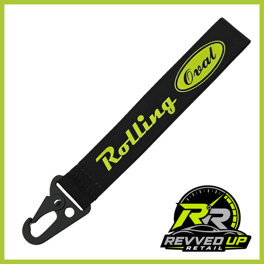 A Rolling Oval brand wristlet strap in black with green printed logos and a black metal carabiner clip, shown on a white background with a Revved Up Retail watermark.